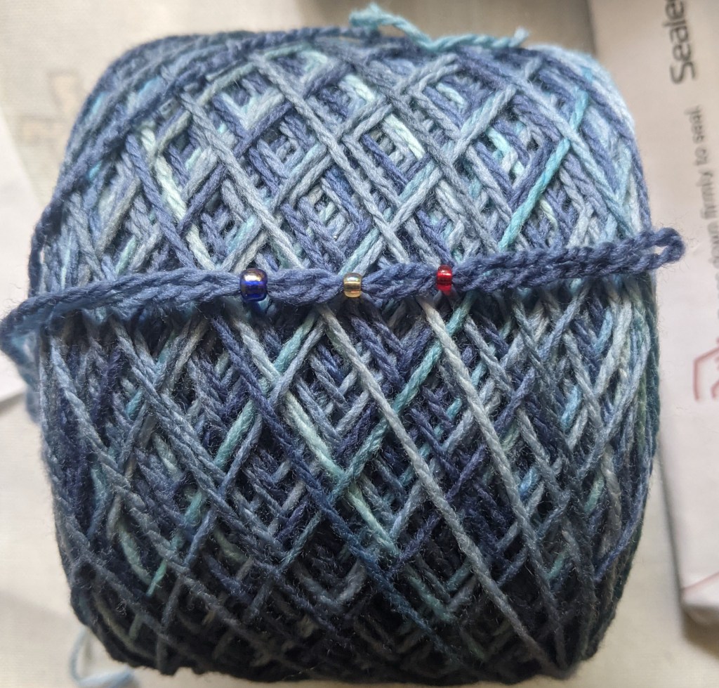 variegated ball of yarn with 3 different coloured and sized beads along a doubled over strand