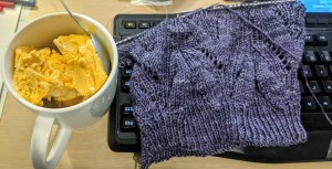 golden brown ice-cream in a mug sitting to the left of a purple knit hat that's about half made.